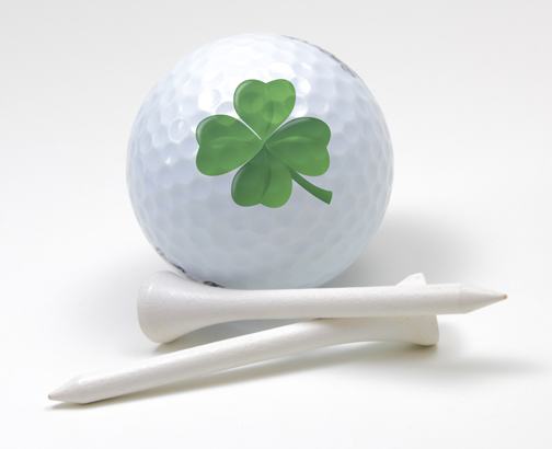 white golf ball with green shamrock leaf imprint and two ball tees below picture. Ireland Golf Cruise.